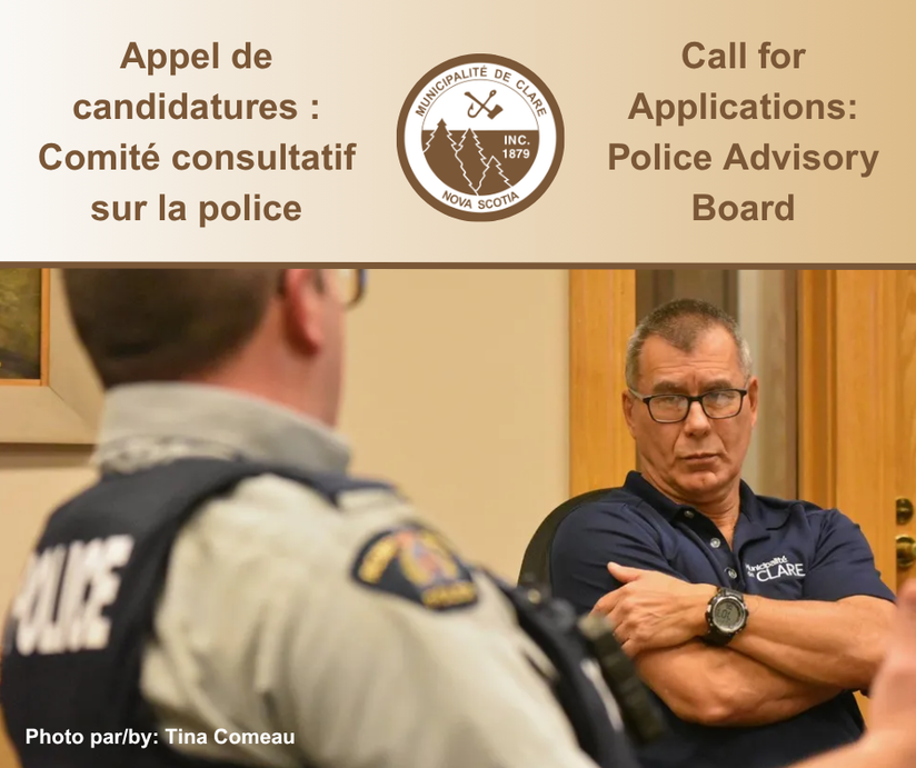 Une photo prise derrière un policier de la GRC assis à une table en conversation avec le conseiller Carl Deveau.